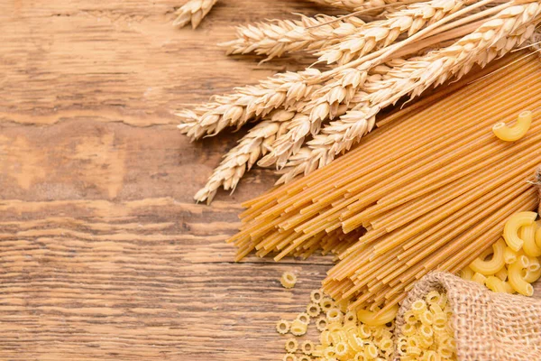 Sacks with different uncooked pasta on wooden table — Stock Photo, Image