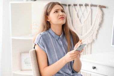 Evde cep telefonu olan endişeli genç bir kadın.