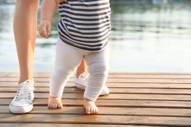 Anne küçük bebeğine nehir kenarında yürümeyi öğretiyor.