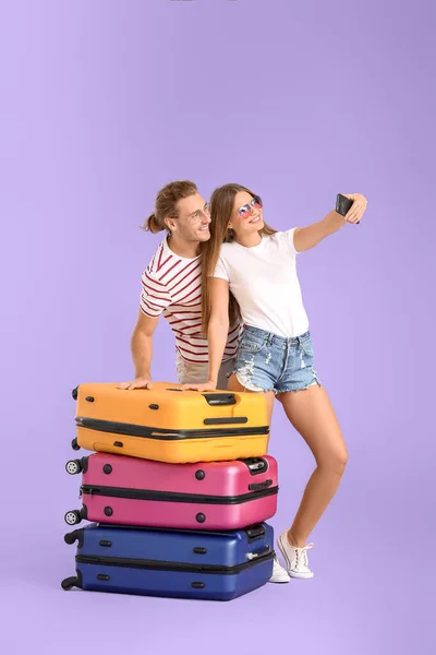 Молодая пара с чемоданами делает селфи на цветном фоне — стоковое фото