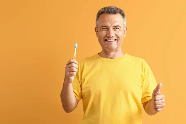 Mature man with toothbrush showing thumb-up on color background — Stock Photo, Image