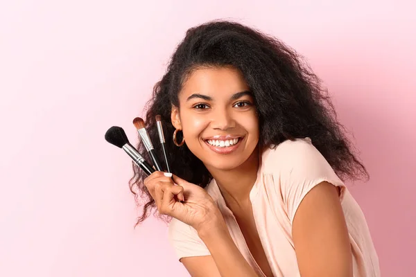 Krásná africko-americká žena s make-up štětce na barevném pozadí — Stock fotografie