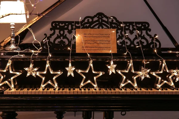 Piano with glowing Christmas garland in room — Stock Photo, Image