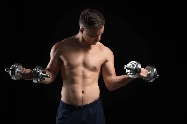 Jóképű férfi testépítő súlyzókkal sötét háttéren — Stock Fotó