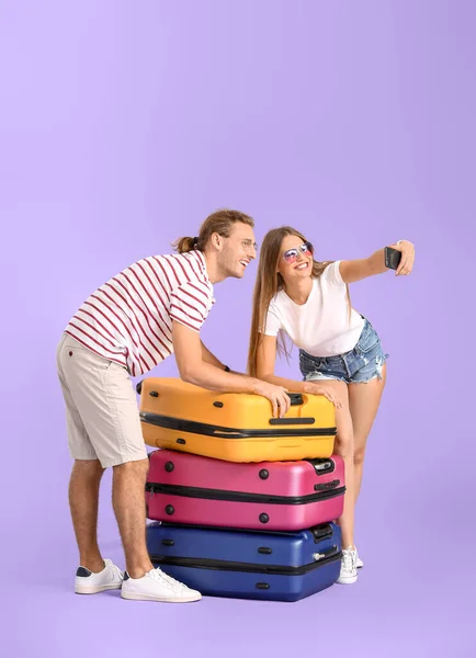 Pareja joven con maletas tomando selfie sobre fondo de color — Foto de Stock