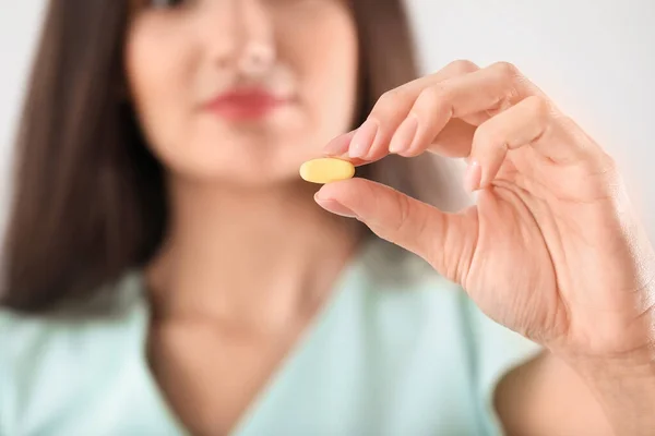 Young woman with pill on light background, closeup — Stock Photo, Image