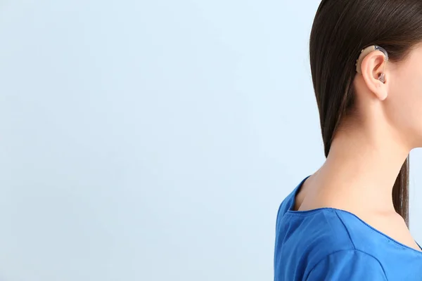 Young woman with hearing aid on color background — Stock Photo, Image