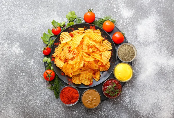 Plate with tasty potato chips, tomatoes and spices on table — Stock Photo, Image