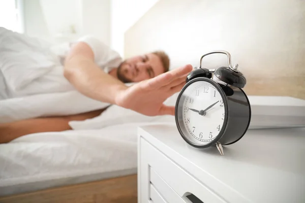 Reggel a fiatalember kikapcsolja az ébresztőórát, miközben alszik az ágyban — Stock Fotó