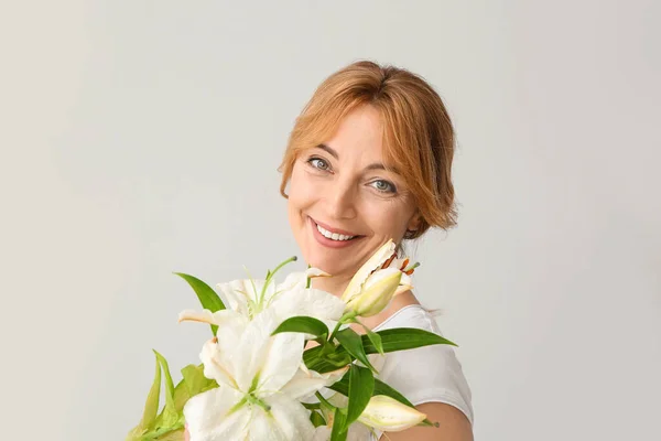 Volwassen vrouw met mooie bloemen op lichte achtergrond — Stockfoto