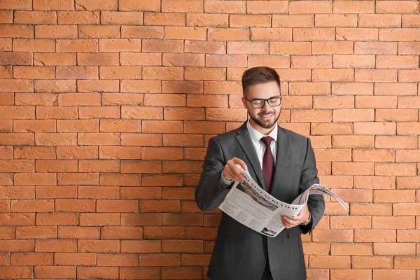 Bonito empresário com jornal contra parede de tijolo — Fotografia de Stock