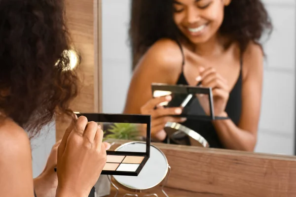 Красивая афроамериканка наносит макияж перед зеркалом — стоковое фото