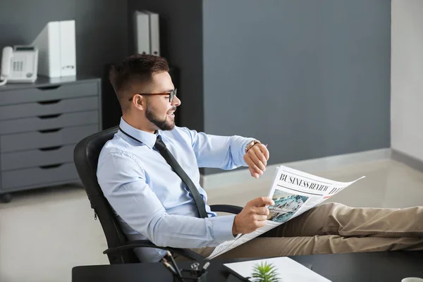 Красивий бізнесмен дивиться на дивіться, читаючи газету в офісі — стокове фото