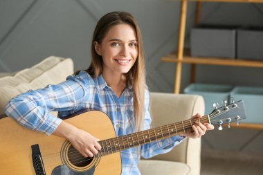 Evde gitar çalan genç bir kadın.