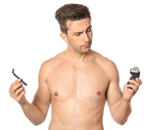 Handsome young man choosing between razor and electric shaver on white background — Stock Photo, Image