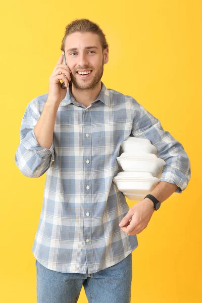 Porträtt av lycklig man med mat behållare talar med mobiltelefon på färg bakgrund — Stockfoto