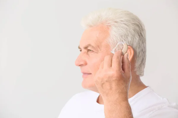 Mature man with hearing aid on light background — Stock Photo, Image
