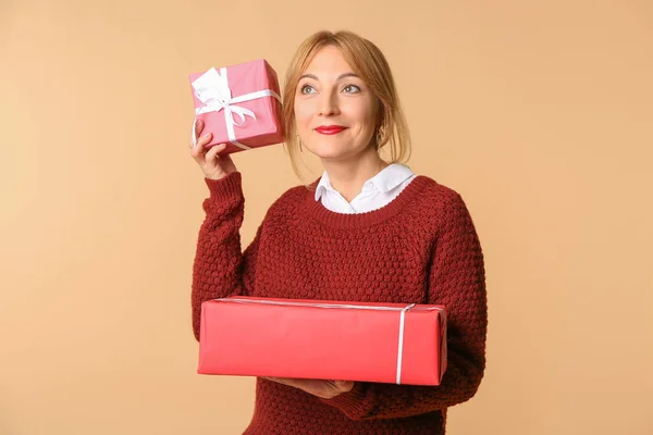 Beautiful mature woman with gift boxes on color background