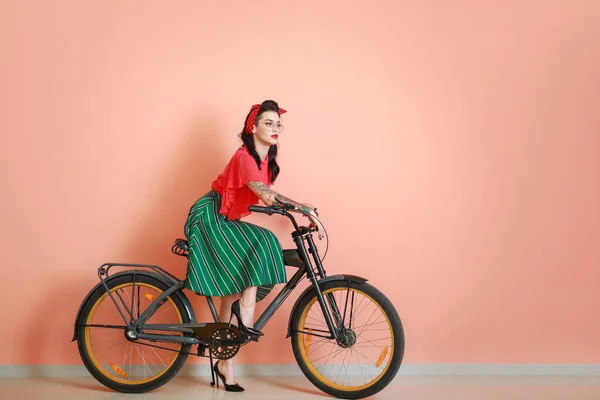 Portrait of beautiful tattooed pin-up woman riding bicycle against color wall — Stock Photo, Image