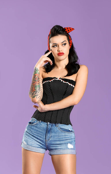 Portrait of beautiful tattooed pin-up woman on color background