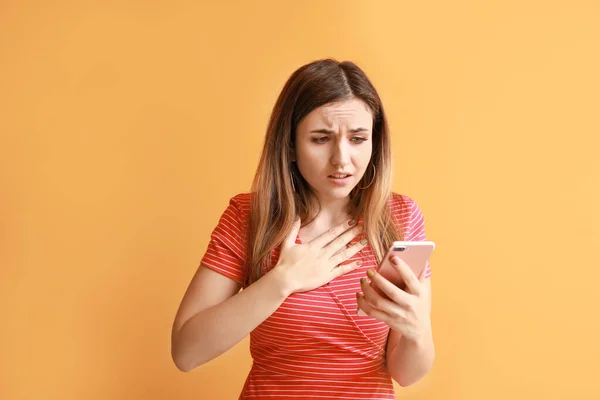 Portrait of worried young woman with mobile phone on color background — Stock Photo, Image