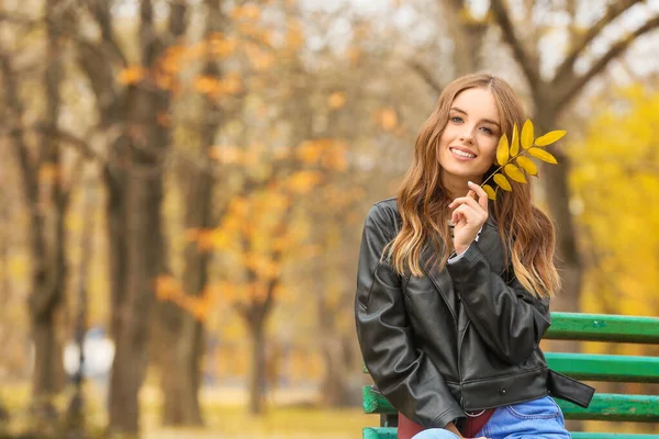 Portrait of stylish young woman sitting on bench in autumn park — Stock Photo, Image