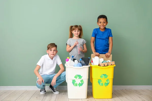Niños pequeños y contenedores con basura cerca de la pared de color. Concepto de reciclaje —  Fotos de Stock