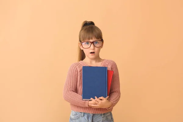 Surprised little girl with books on color background — Stock Photo, Image