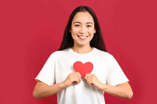 Beautiful young Asian woman with paper heart on color background — ストック写真