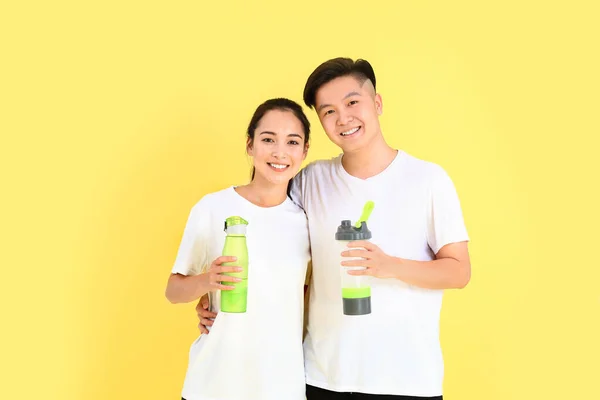 Sporty young Asian couple with bottles of water on color background — Stock Photo, Image