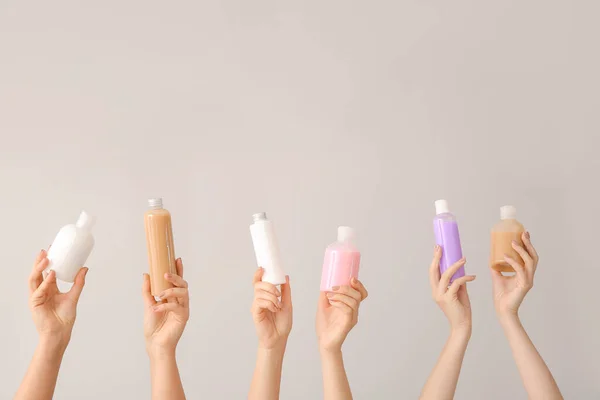 Жіночі руки з різними косметичними продуктами в пляшках на сірому фоні — стокове фото