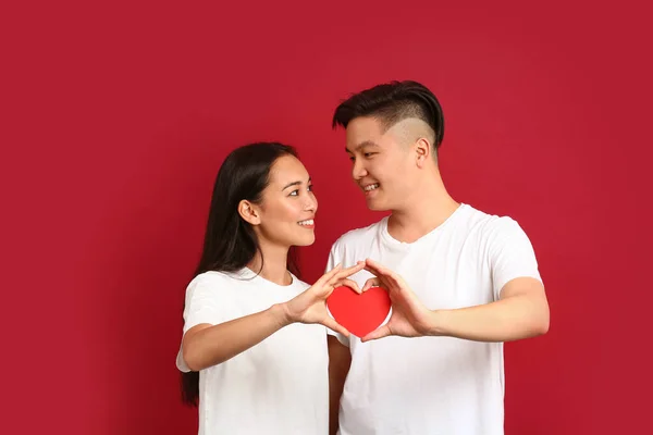 Happy young Asian couple with paper heart on color background — Stock Photo, Image