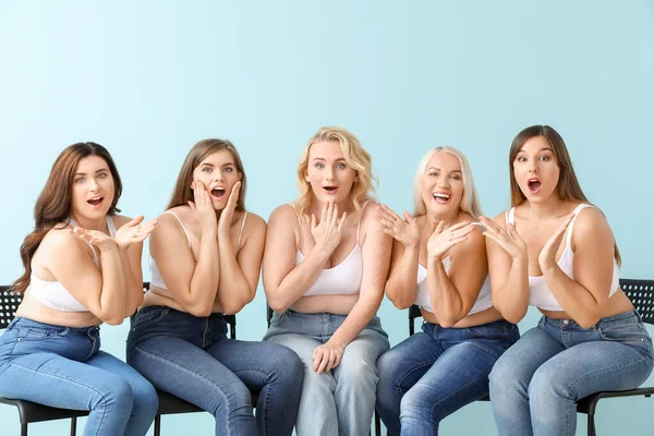 Group of surprised body positive women sitting on chairs against color background — ストック写真