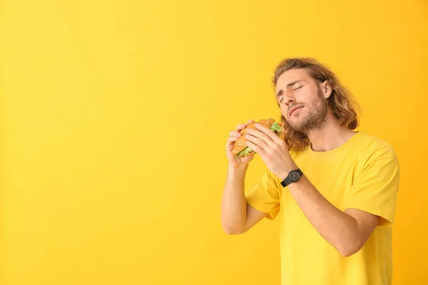 Portrait of happy man with tasty sandwich on color background — Stock Photo, Image