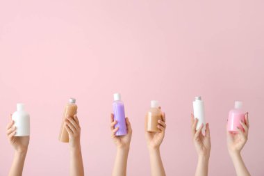 Farklı kozmetik ürünlere sahip kadın elleri renkli arka planda şişelerde