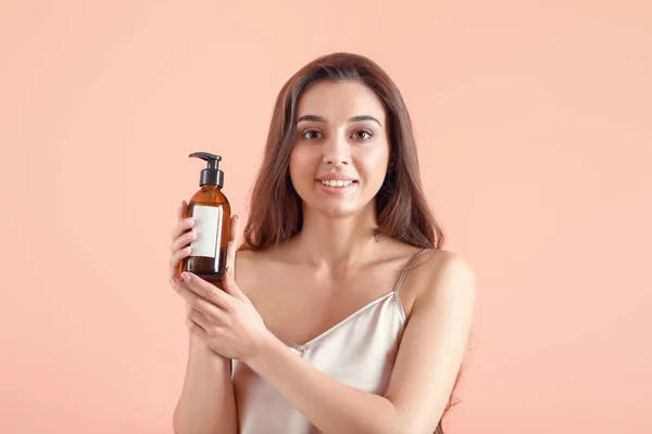 Beautiful young woman with bottle of cosmetics on color background — Stock Photo, Image