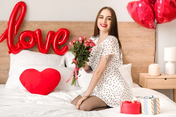 Hermosa joven con regalos y flores en el dormitorio. Celebración de San Valentín — Foto de Stock