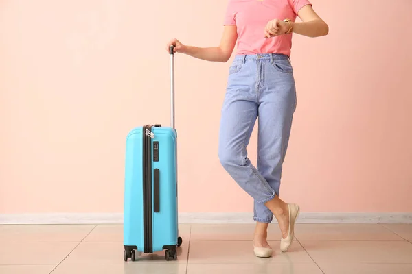 Mulher com mala olhando para relógio perto de parede de cor. Conceito de viagem — Fotografia de Stock