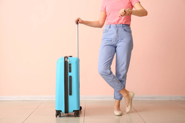 Woman with suitcase looking at watch near color wall. Travel concept