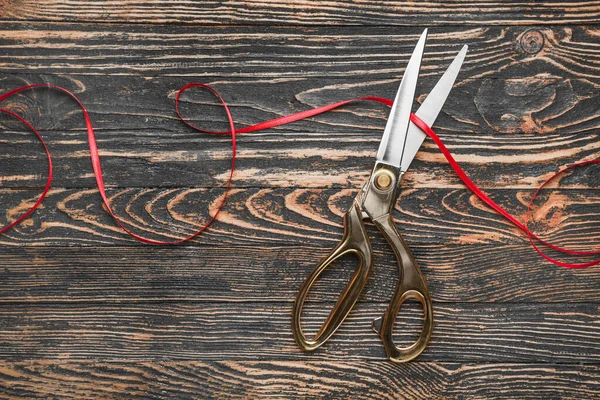 Scissors and red ribbon on wooden background