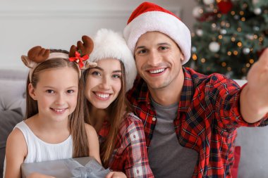 Mutlu genç aile Noel arifesinde evde selfie çekiyor.
