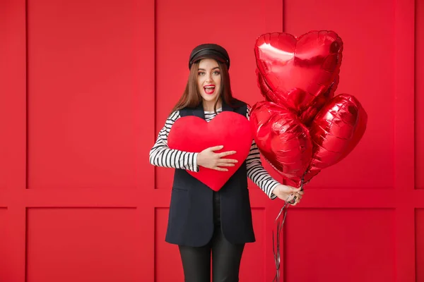 Beautiful young woman with big red heart and balloons on color background. Valentine's Day celebration — ストック写真