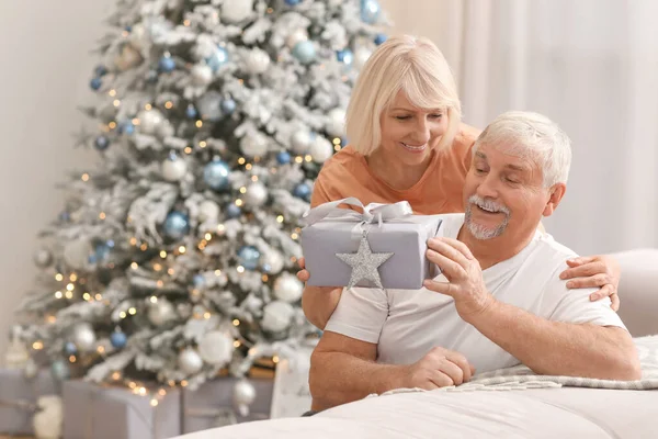 Mature woman greeting her husband with Christmas gift at home — Stock Photo, Image