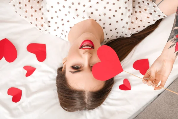 Beautiful young woman with red hearts lying on bed. Valentine's Day celebration — Stock Photo, Image