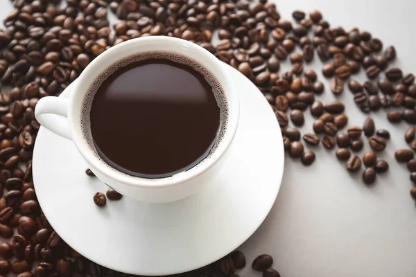 Cup of hot coffee with beans on light background — Stock Photo, Image