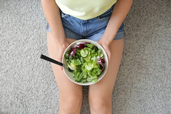 Mujer con ensalada de verduras saludables en un tazón sentado en el suelo — Foto de Stock