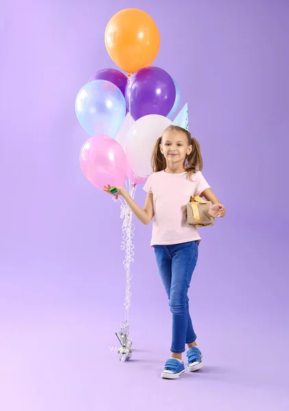 Kleines Mädchen mit Geburtstagsgeschenk und Party-Gebläse auf farbigem Hintergrund — Stockfoto