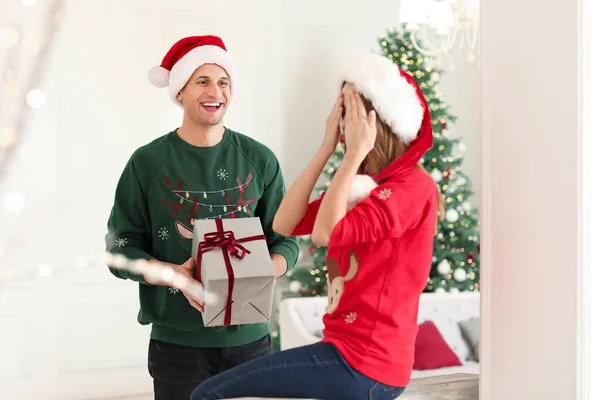 Happy young man giving Christmas present to his girlfriend at home — Stock Photo, Image