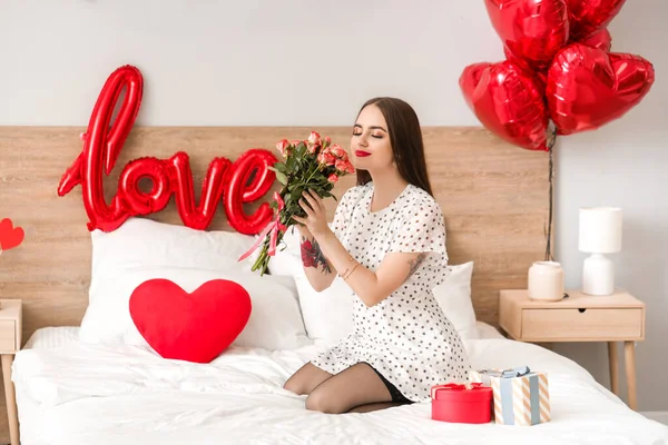 Hermosa joven con regalos y flores en el dormitorio. Celebración de San Valentín — Foto de Stock