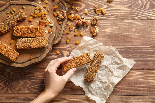 Woman taking tasty granola bar from table — Stock Photo, Image